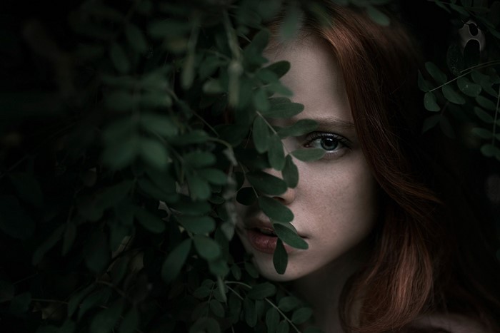 Woman with red hair peeking through green leaves