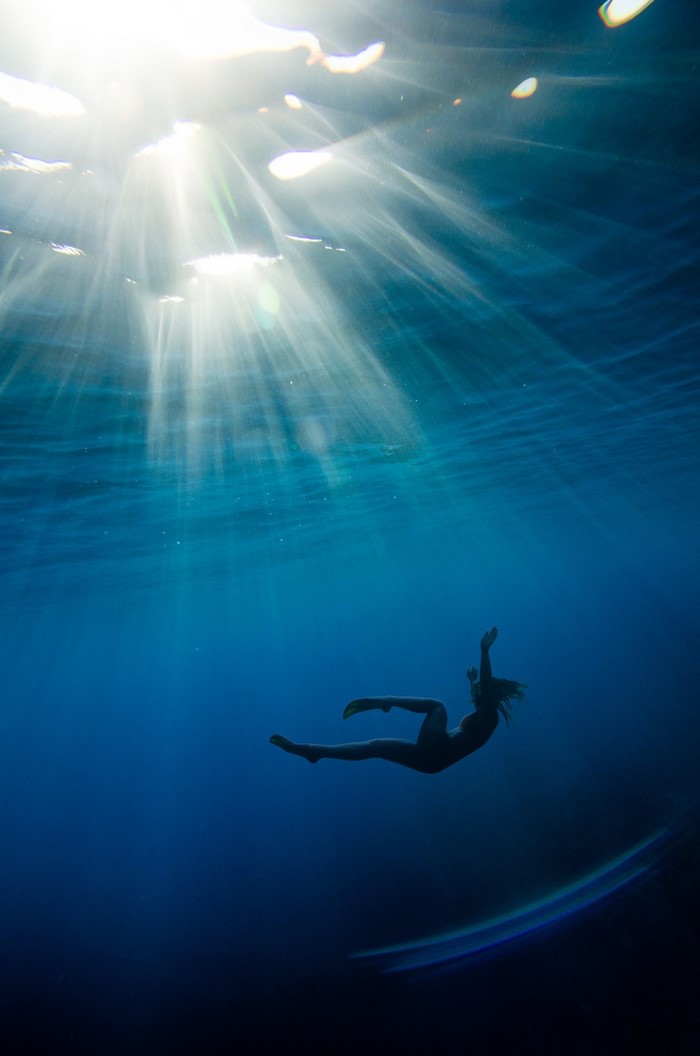 Woman freediving underwater with sun rays
