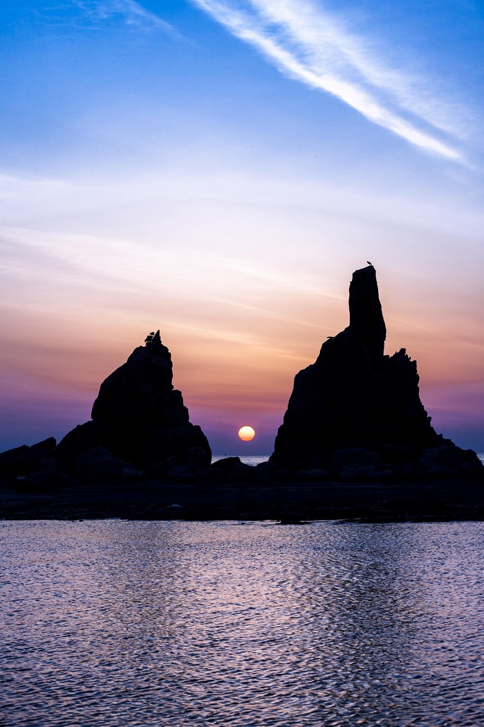 Silhouette of rocks and sun over the sea at sunset
