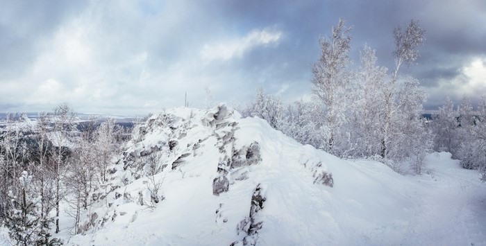 Snow-covered rocky ridge with frosted trees under cloudy sky