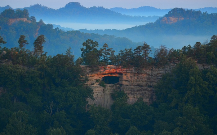 Natural rock arch with glowing opening in forested mountains