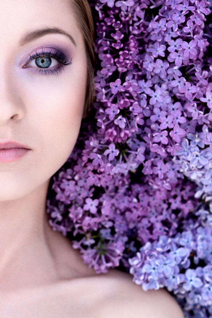 Woman with blue eyes and purple makeup near lilacs