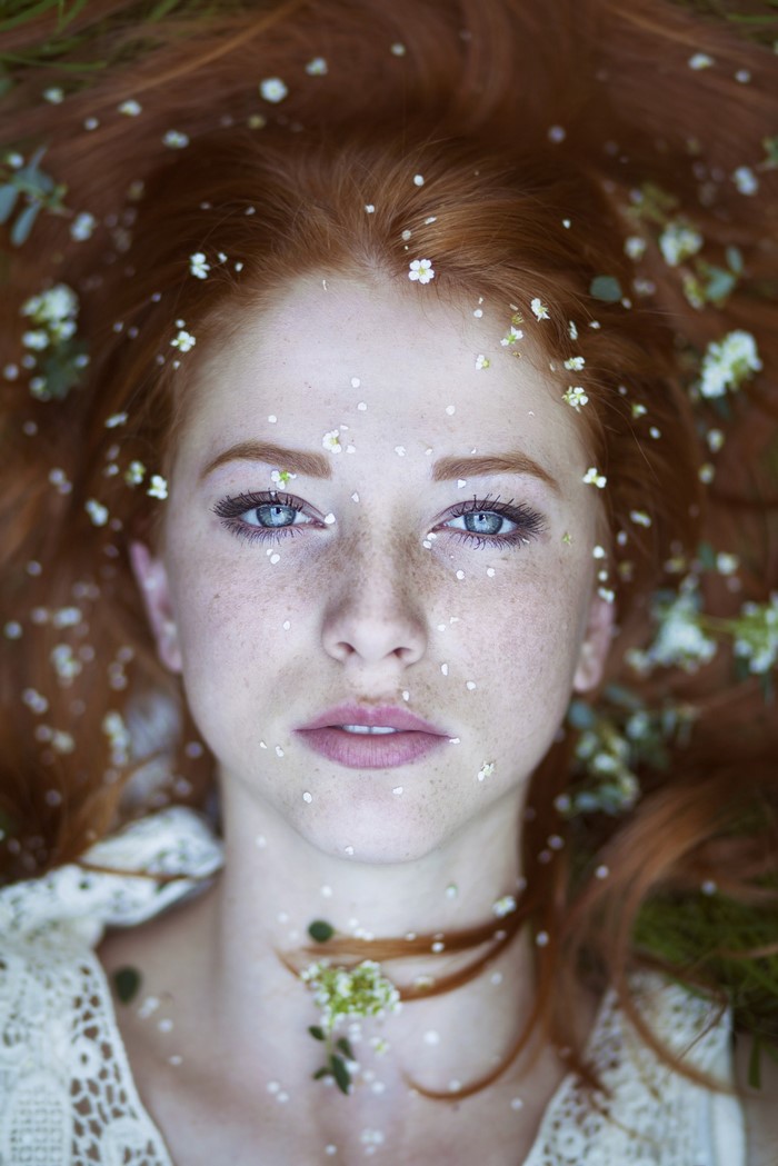 Redhead woman with blue eyes and freckles covered in flowers