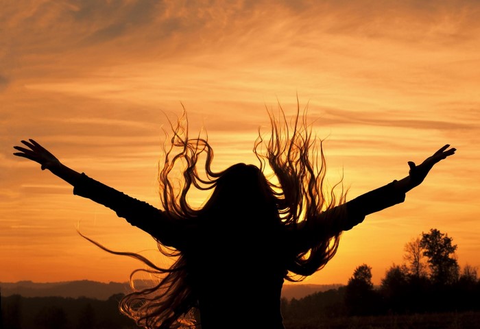 Silhouette of a woman with arms outstretched at sunset