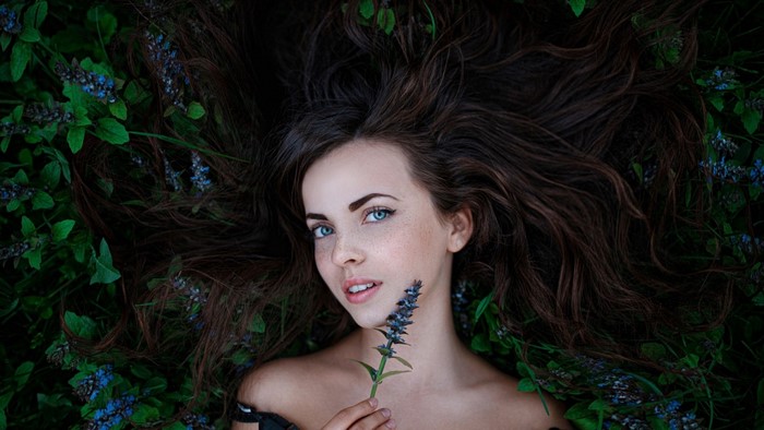 Woman with blue eyes and freckles lying in flowers