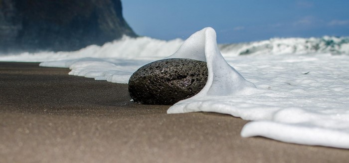 Rock on a black sand beach with waves