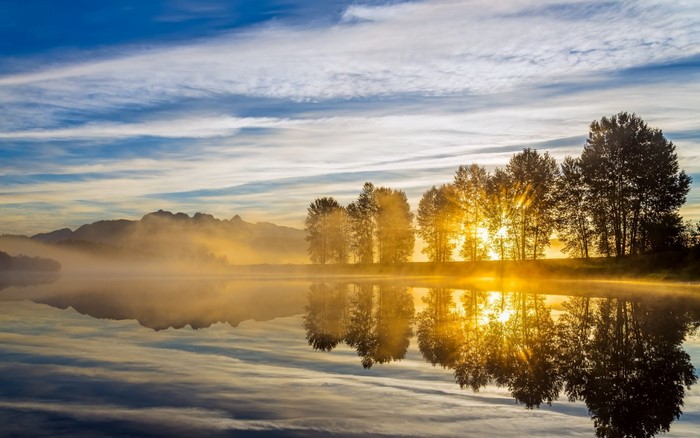 Sunrise over misty lake with trees and mountains