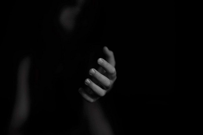 Monochrome image of a hand reaching out of darkness