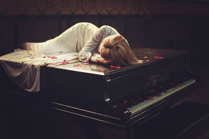 Woman in white dress lying on a piano with rose petals
