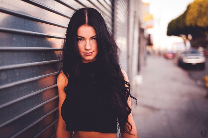 Woman with long black hair leaning against a wall