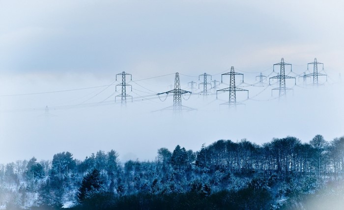 Transmission towers in mist over a snowy forest