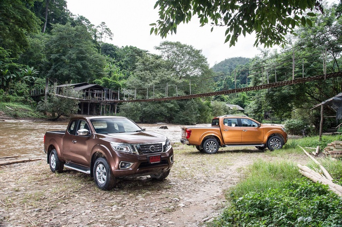 Two Nissan Navara NP300 pickup trucks parked near a river and a suspension bridge