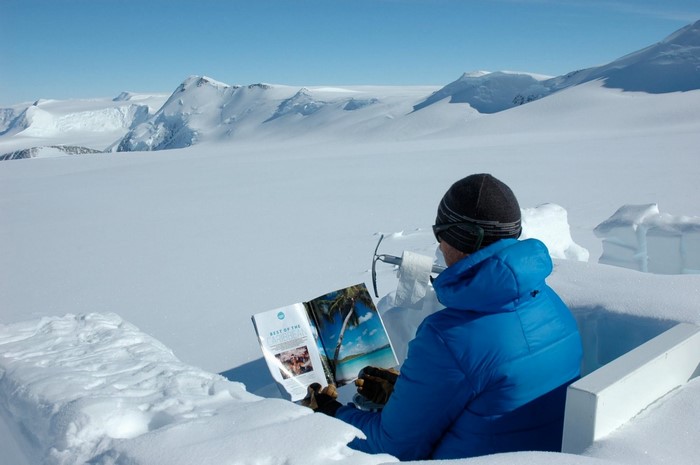 Man reading a magazine in a snow fort with mountains