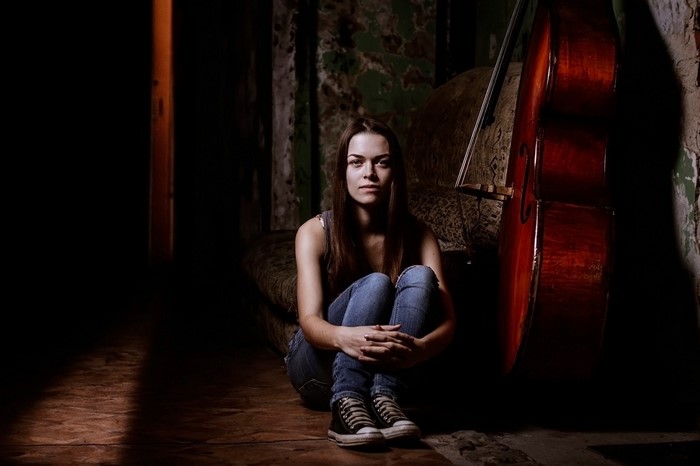 Woman sitting next to a cello in a dark room