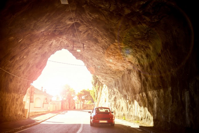 Red Porsche 911 driving out of a rock tunnel