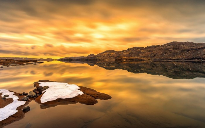 Sunset over a calm lake with mountains and snow-capped rocks