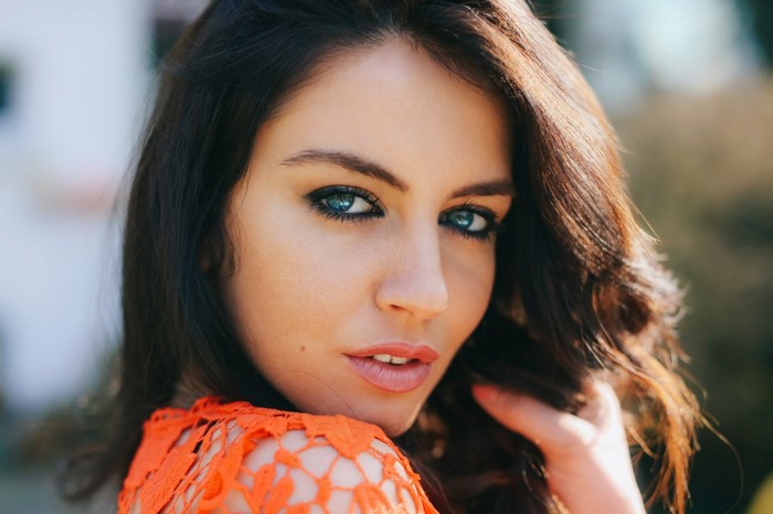 Aurela Skandaj portrait with blue eyes and orange top