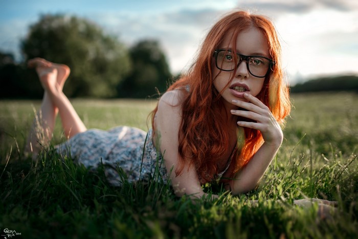 Redhead woman with glasses lying in grass