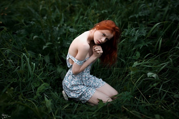 Redhead woman in floral dress kneeling in grass
