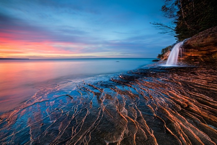Waterfall cascading onto rocky shore at sunset