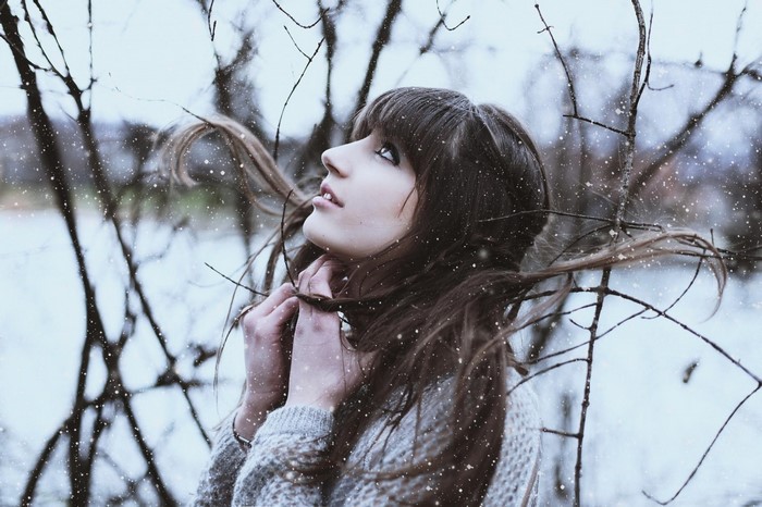 Woman in sweater looking up in winter with snow
