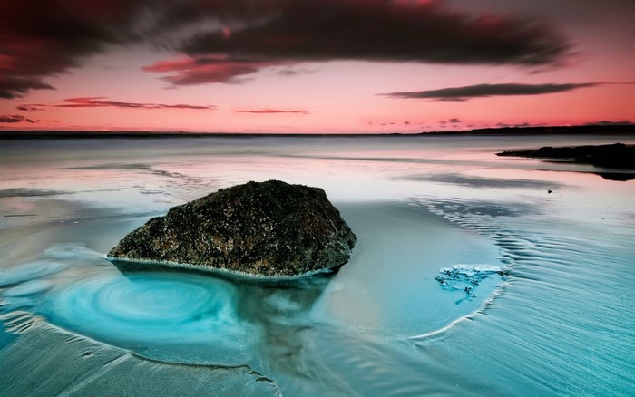 Long exposure sunset over a rocky beach with swirling water