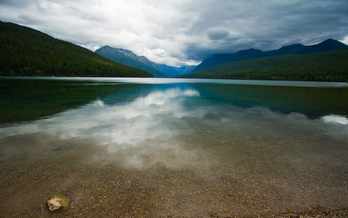 Lake reflection with mountains and forest under cloudy sky