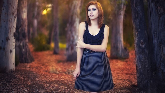 Woman with red hair in a black dress in a forest