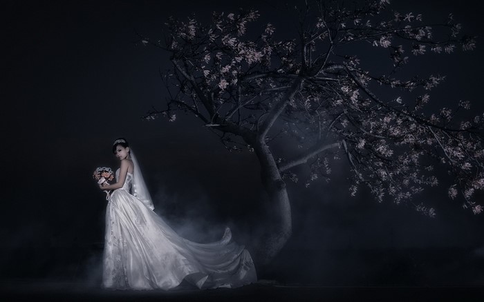 Bride holding bouquet under a tree at night