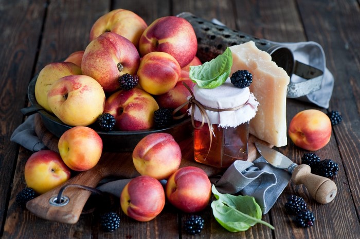 Peaches, blackberries, cheese, and honey on a wooden surface