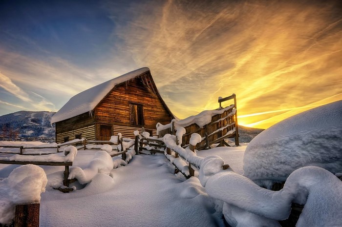 Wooden barn in snow during sunset