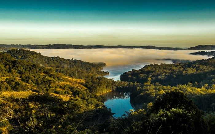 Misty lake surrounded by forested hills at sunrise