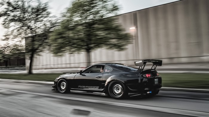 Black Toyota Supra with large rear wing driving on road