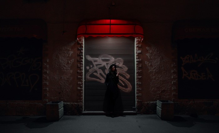 Woman in black dress standing at night in front of a shuttered storefront