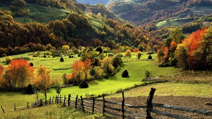 Autumn landscape in a mountainous valley with haystacks and a wooden fence