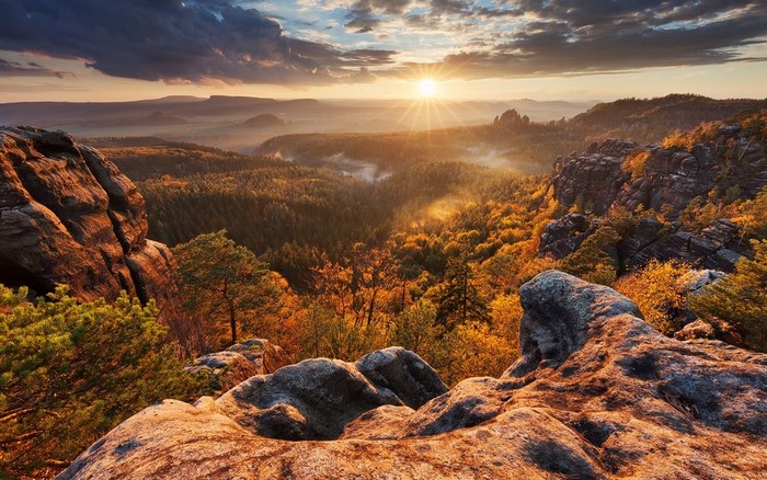 Sunrise over a misty autumn forest valley with rocky outcrops