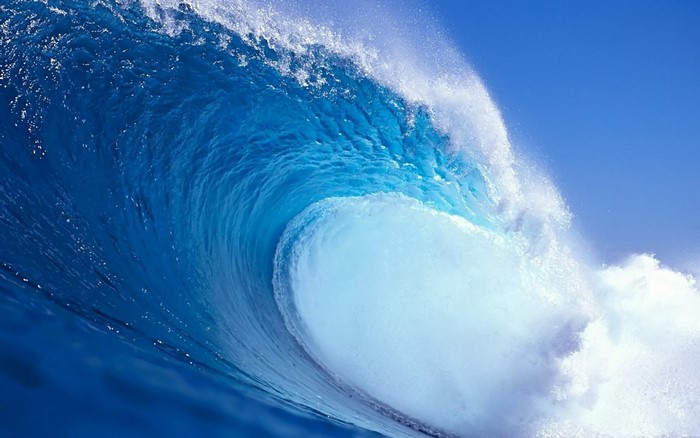 A large blue ocean wave crests and breaks
