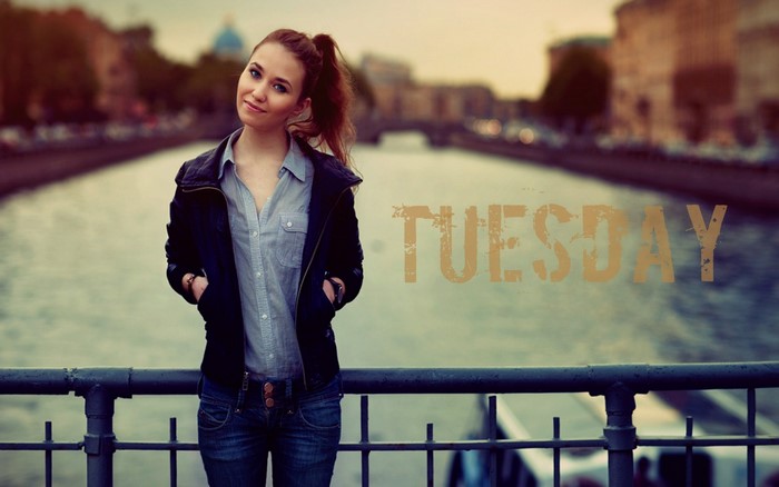 Girl in jacket and jeans standing by a river with text Tuesday