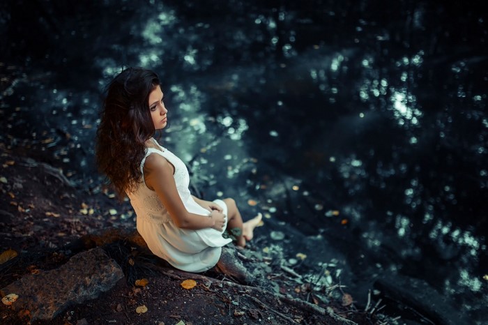 Woman in white dress sitting by dark water