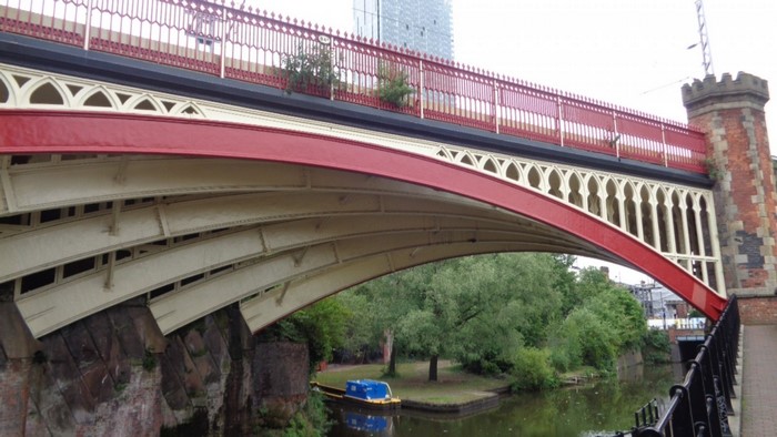 Red and white arch bridge over a canal with a blue boat