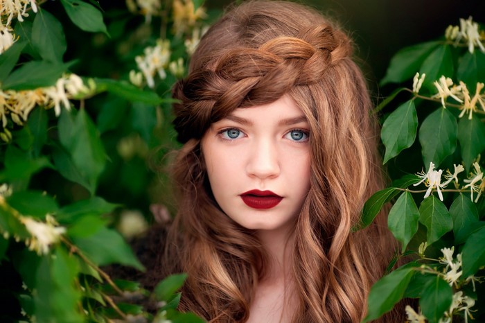 Young woman with braided hair and blue eyes surrounded by foliage