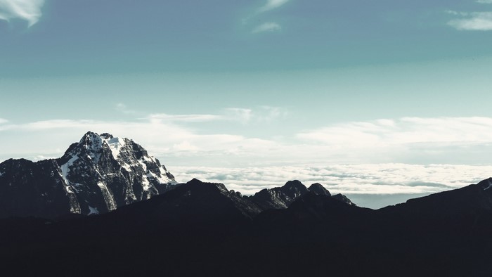 Snow-capped mountain peak above clouds and dark mountain range