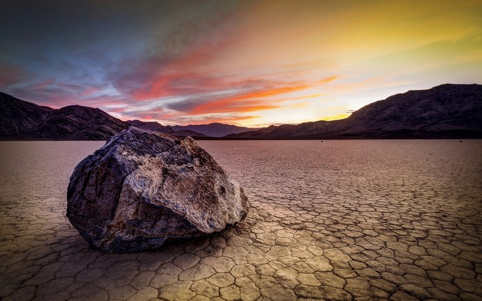 Rock on cracked earth at sunset with mountains