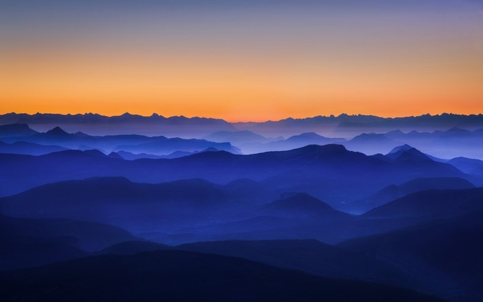 Mountain range at sunset with orange sky and blue mist