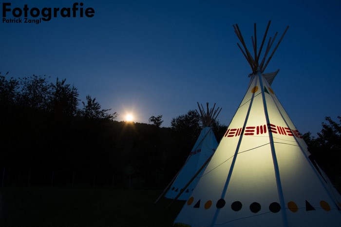 Two illuminated teepees at night with a moonlit sky
