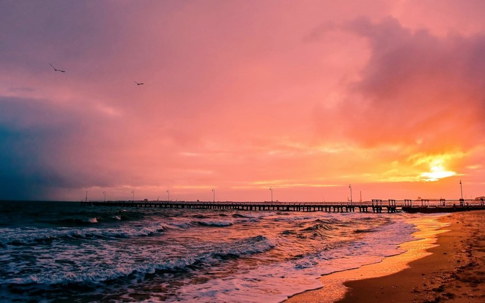 Sunset over the ocean with a pier and waves
