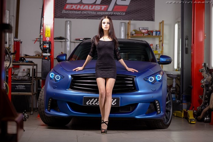 Woman in black dress posing with blue Infiniti car in garage