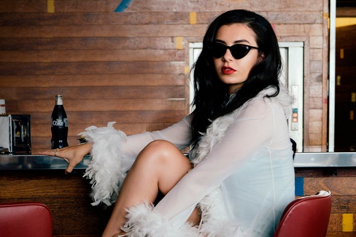 Charli XCX wearing sunglasses and a white feathered dress