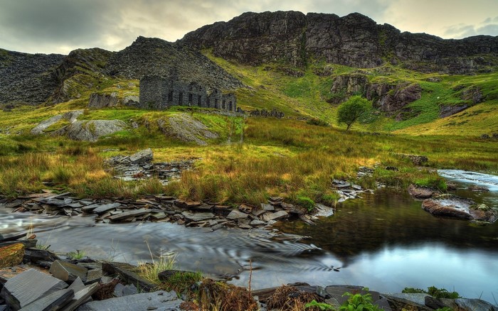 Abandoned stone building in a rocky, mountainous landscape with a stream