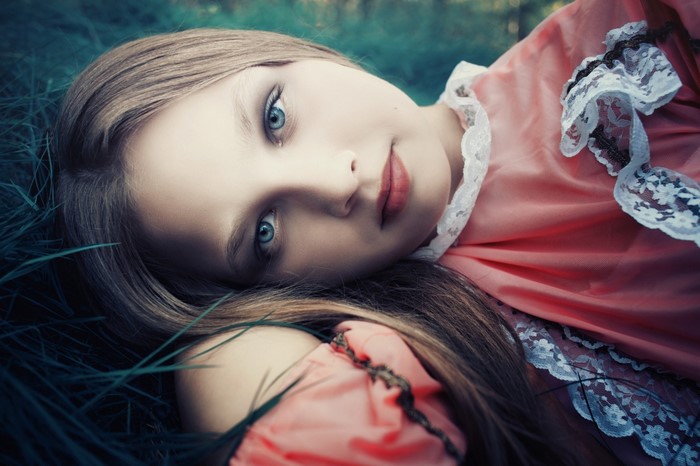 Girl with blue eyes lying in grass wearing pink dress